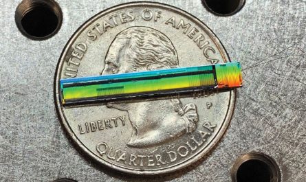 A rainbow-hued strip with black markings on it sits atop a U.S. quarter